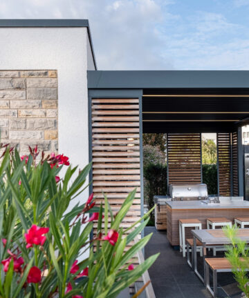 Moderne überdachte Terrasse mit Außenküche, Sitzgruppe und Feuerstelle mit Orleander und Schmuckkörbchen